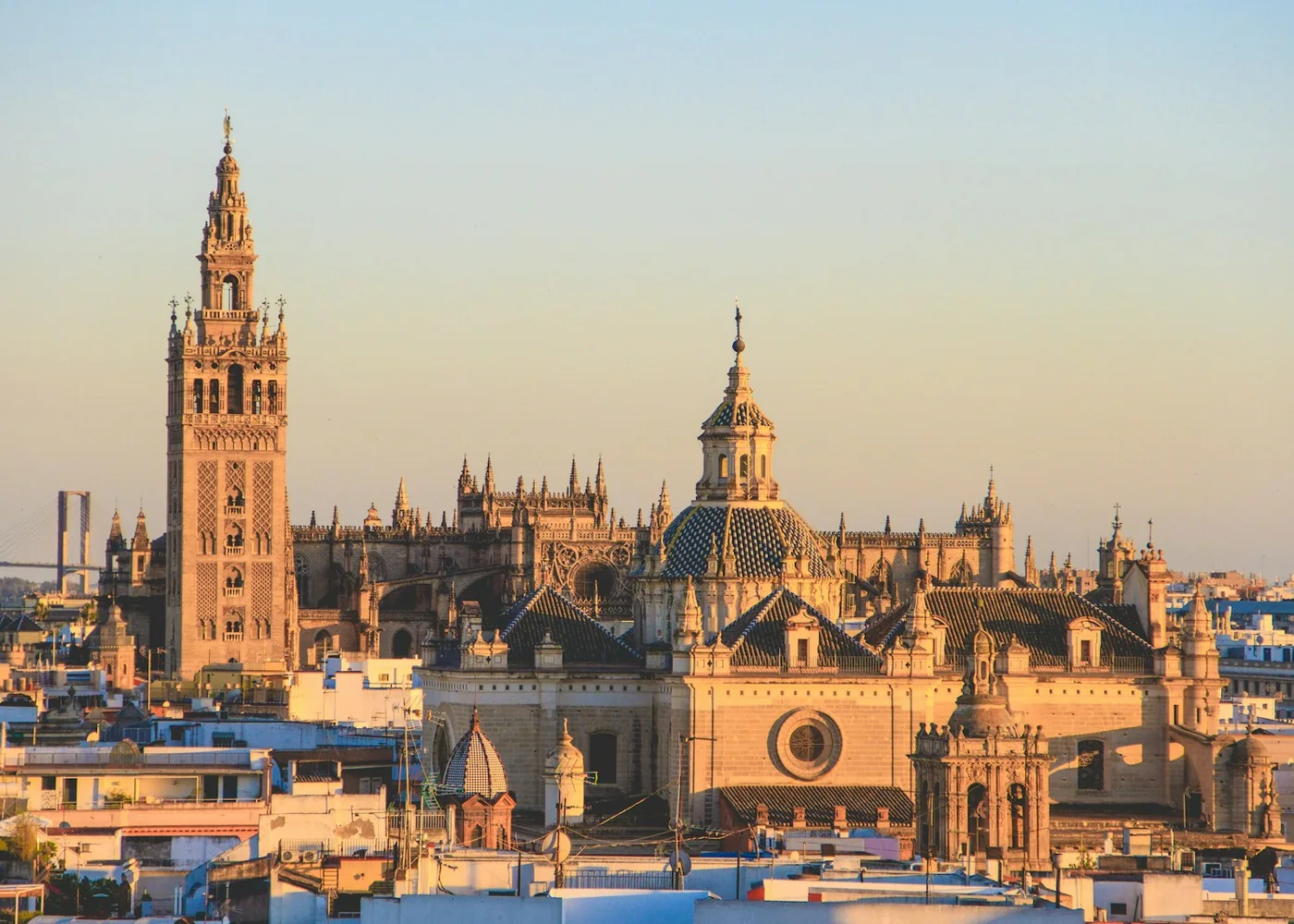 The Giralda tower and Seville Cathedral rising above the rooftops of Seville's old town at sunset (representative photograph of Seville's historic centre, across the river from Isla de la Cartuja)