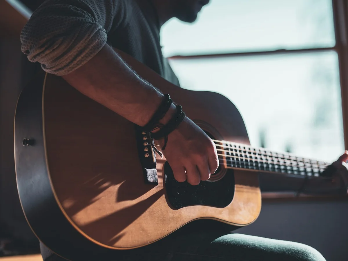 A guitarist's hand plucking the strings of an acoustic guitar in close-up, warm window light behind (representative photograph of flamenco guitar, not El Palacio Andaluz's own guitarists)
