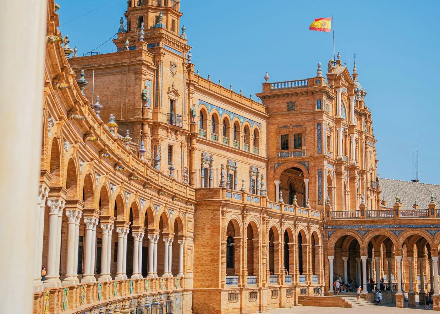 The tiled, curved arcade and towers of the Plaza de España in Seville under a blue sky (representative photograph of Seville's azulejo tilework, not El Palacio Andaluz's own décor)